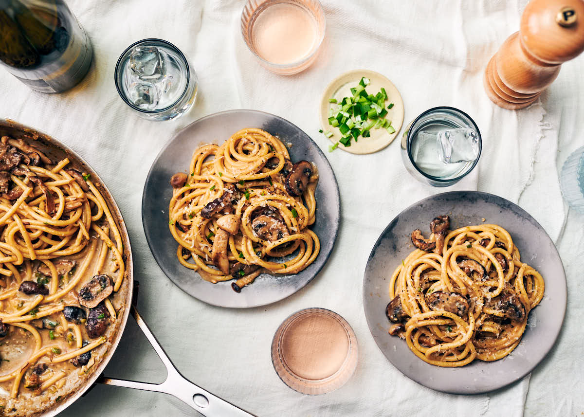 The best mushroom miso pasta on plates and in a skillet on a dining table with wine.