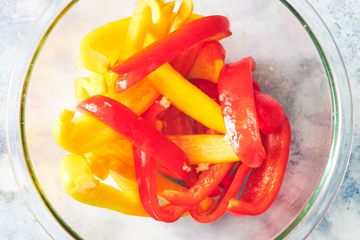 Sliced red and yellow bed peppers in a bowl with olive oil and garlic.