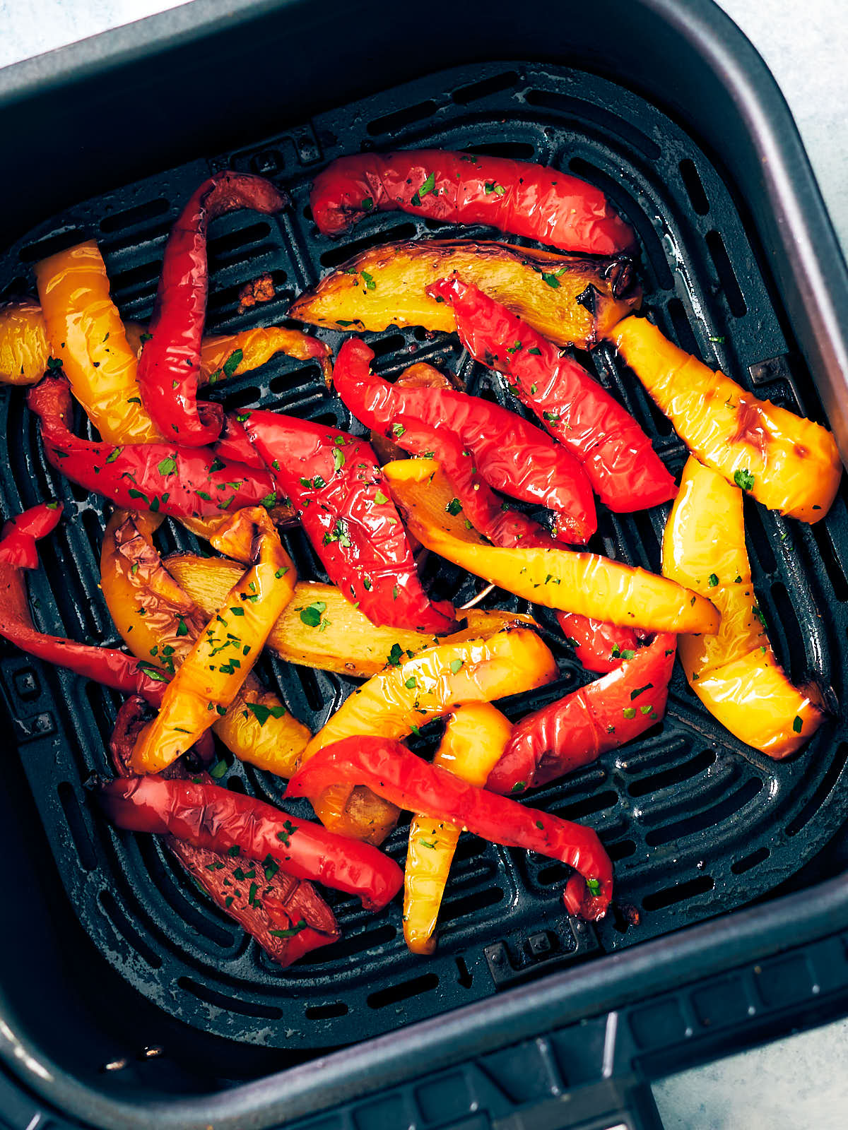 Red and yellow bell peppers in an air fryer basket.