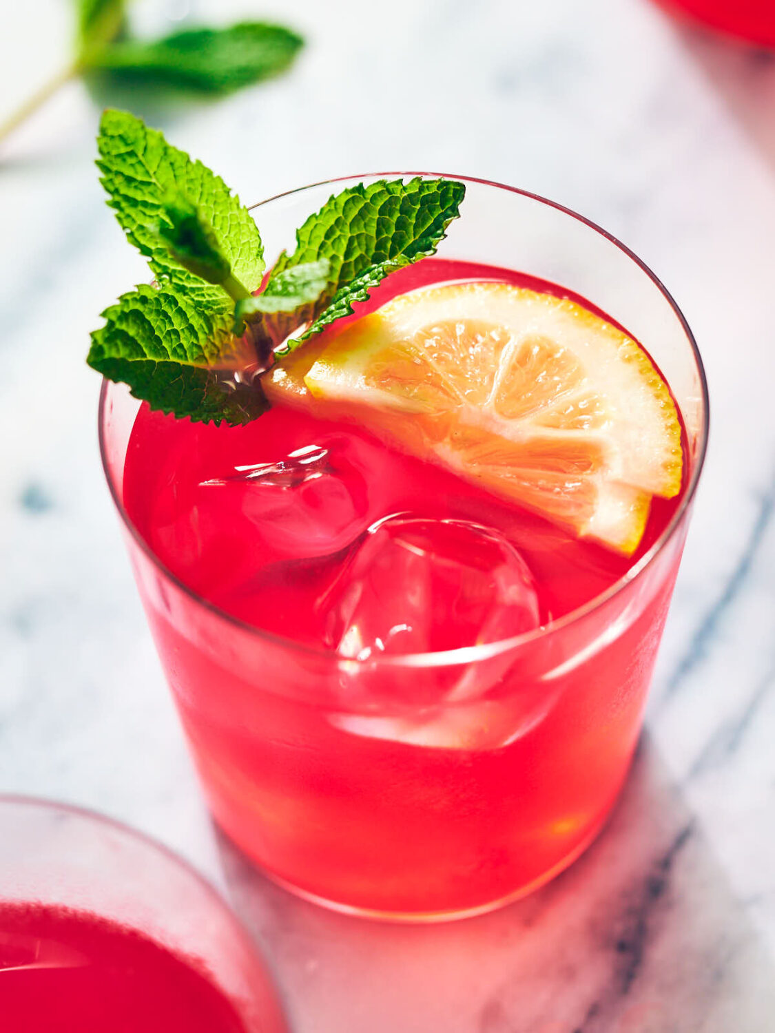 Hibiscus lemonade in a glass with ice, lemon, and mint.