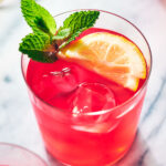 Hibiscus lemonade in a glass with ice, lemon, and mint.