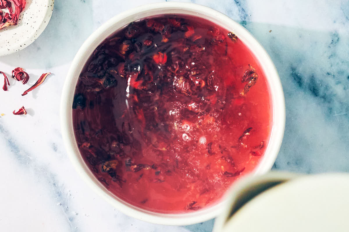 Pouring hot water into a bowl of dried hibiscus and sugar for lemonade recipe.