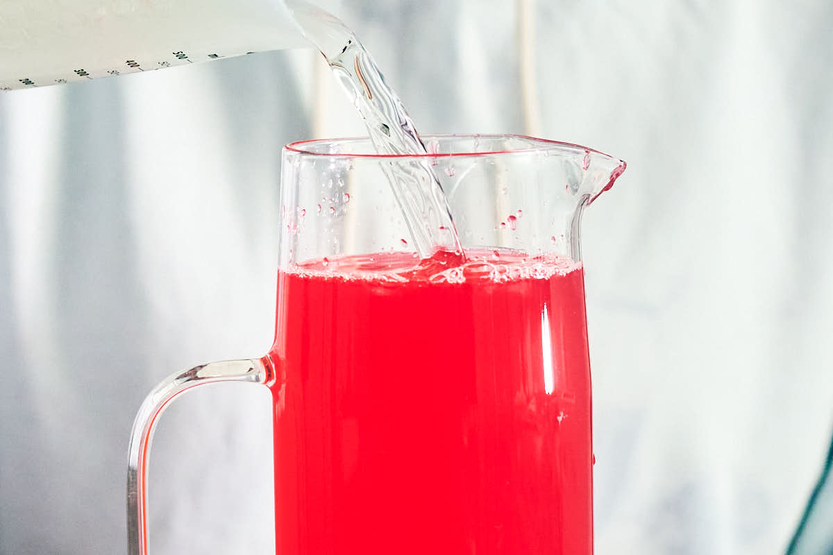 Water being poured into a glass pitcher of hibiscus lemonade.