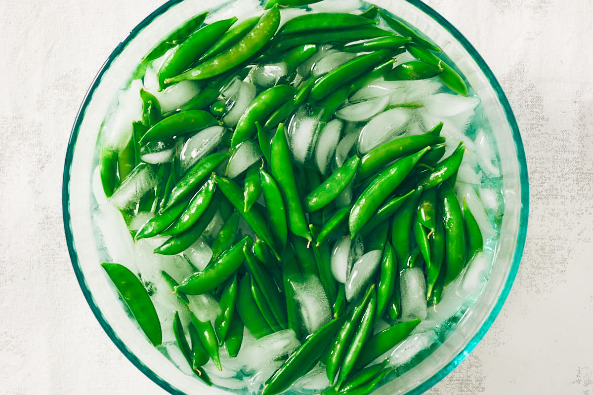 Blanching sugar snap peas in a bowl of ice water after boiling.
