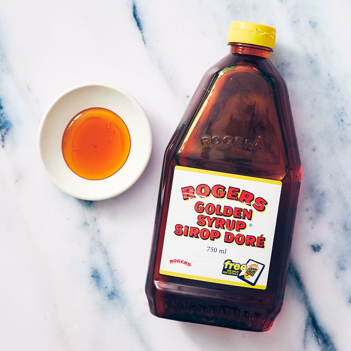 Golden Corn Syrup in a bottle and in a small bowl on marble counter.