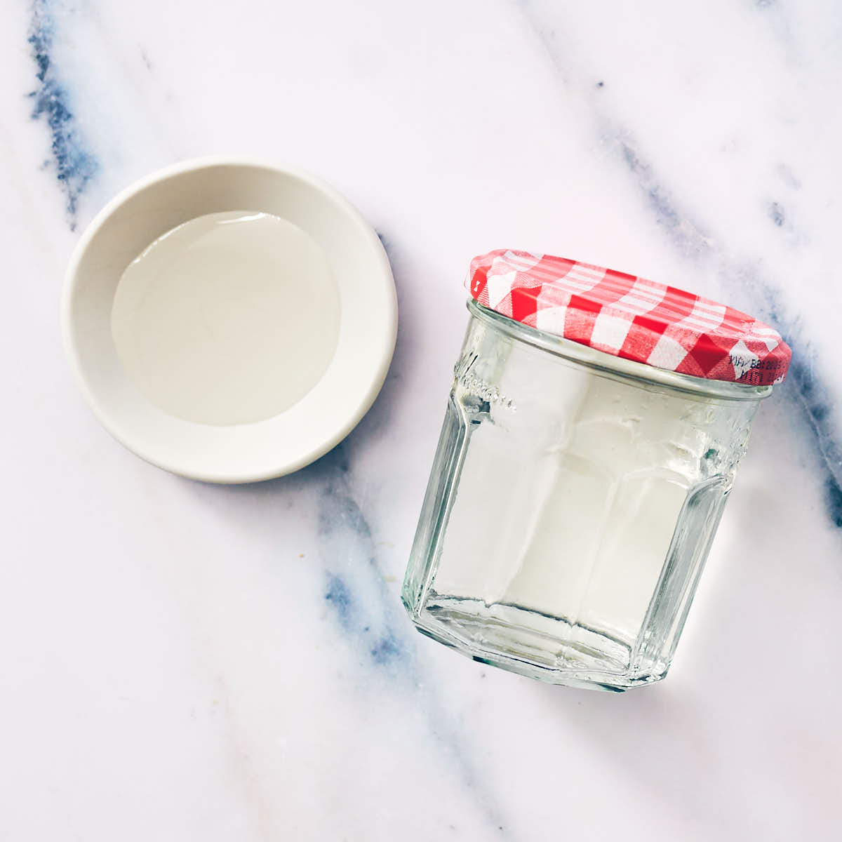Simple syrup in a glass jar and bowl on marble counter.