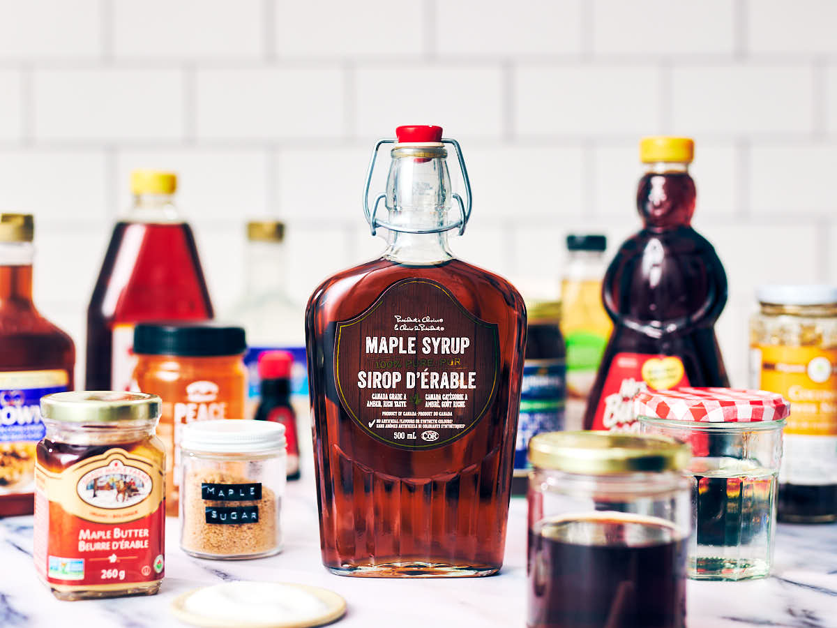 Maple syrup and maple syrup substitutes in bottles and jars on a kitchen counter.