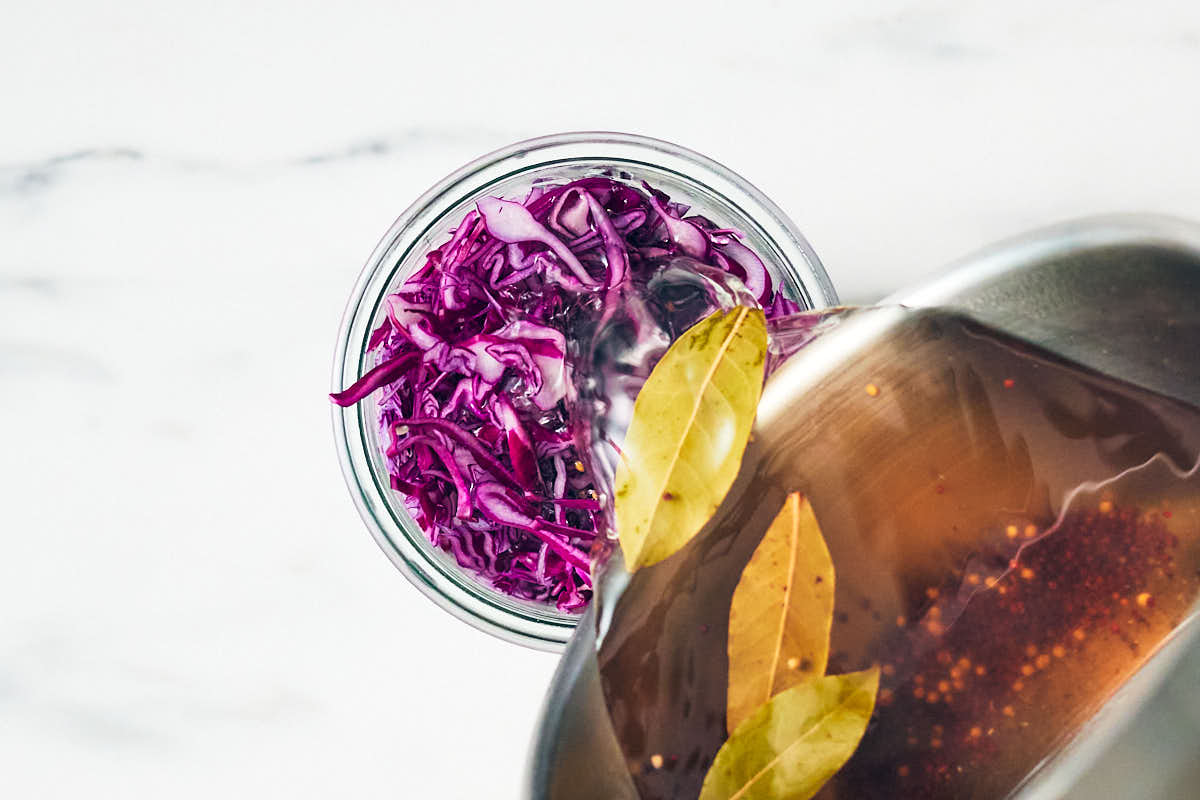 Pouring pickling brine with spices into a jar of red cabbage.