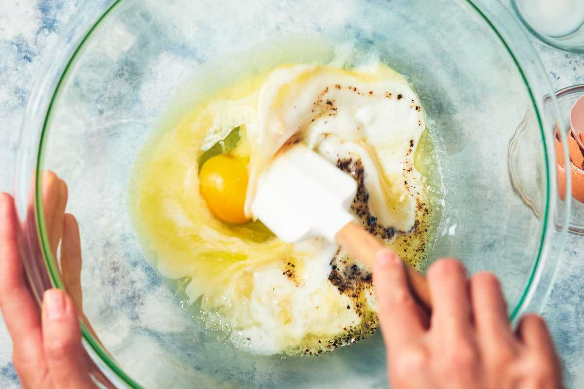 A stirring spoon mixing eggs, milk, and seasonings in a bowl. 