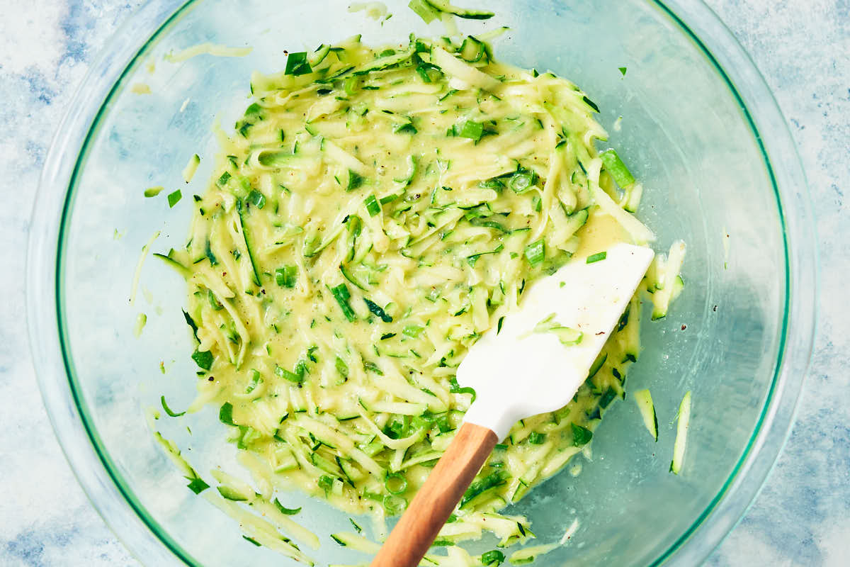 Batter for zucchini muffins in a bowl with a stirring spoon.