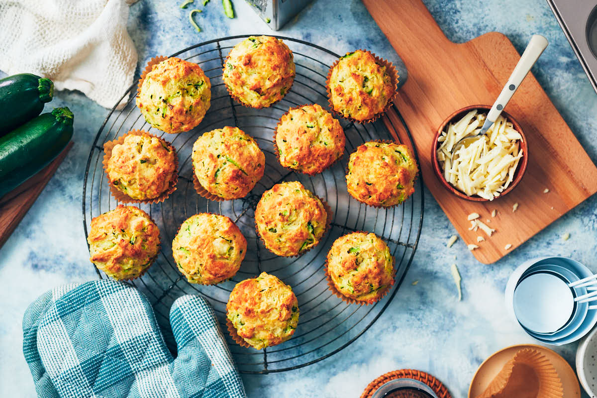 One bowl savory zucchini muffins on a cooling rack with oven mitt.