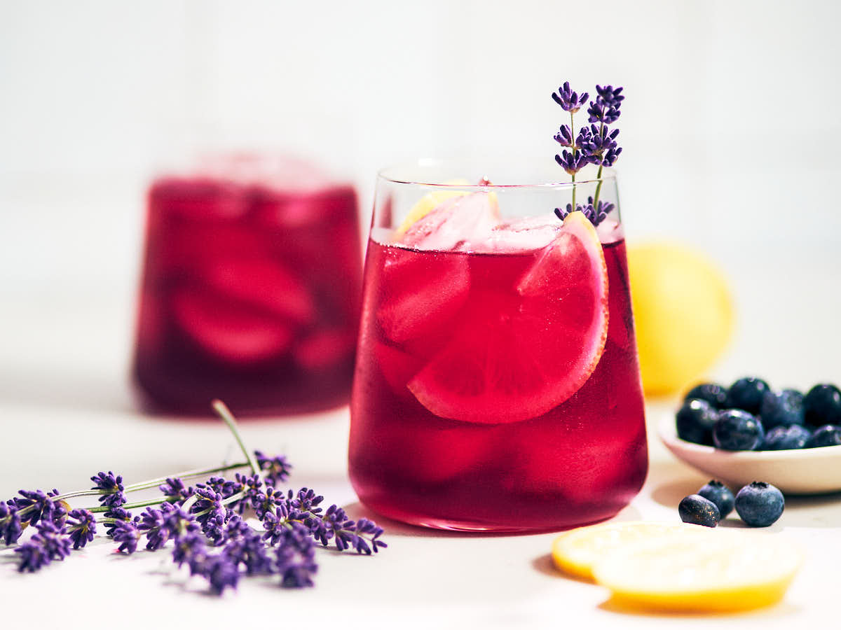 Two glasses of lavender blueberry lemonade on a kitchen counter.