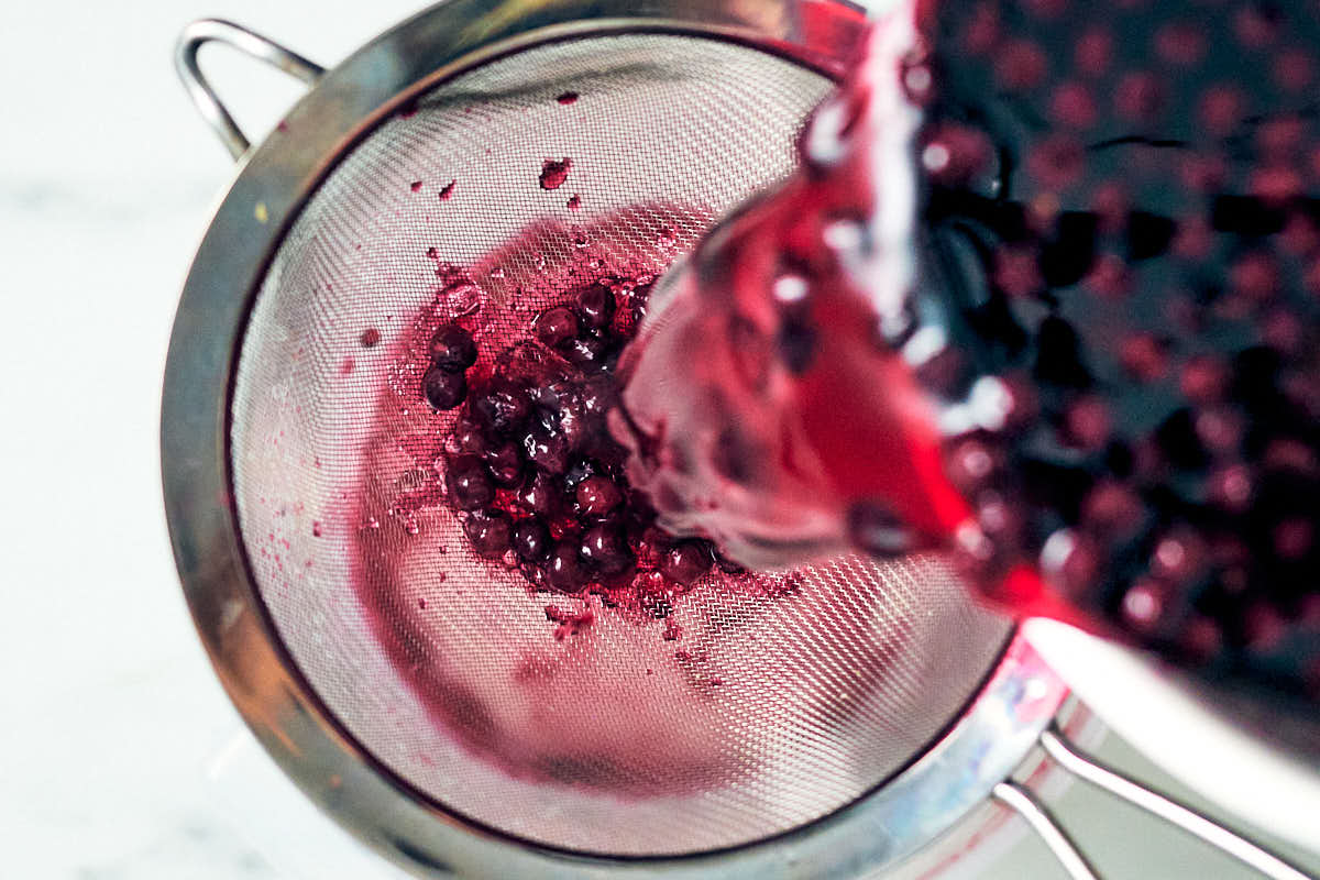 Pouring lavender blueberry simple syrup through a strainer to make lemonade.