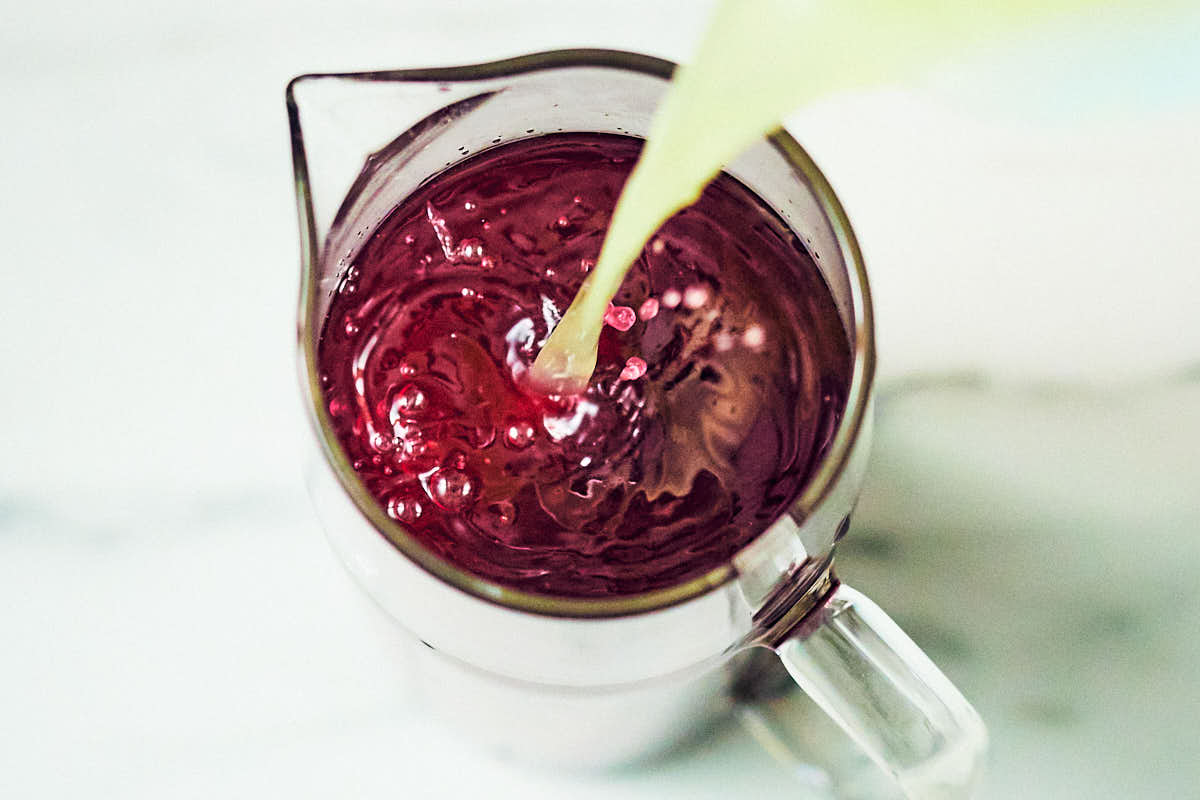Pouring lemon juice into a pitcher of blueberry lavender lemonade.