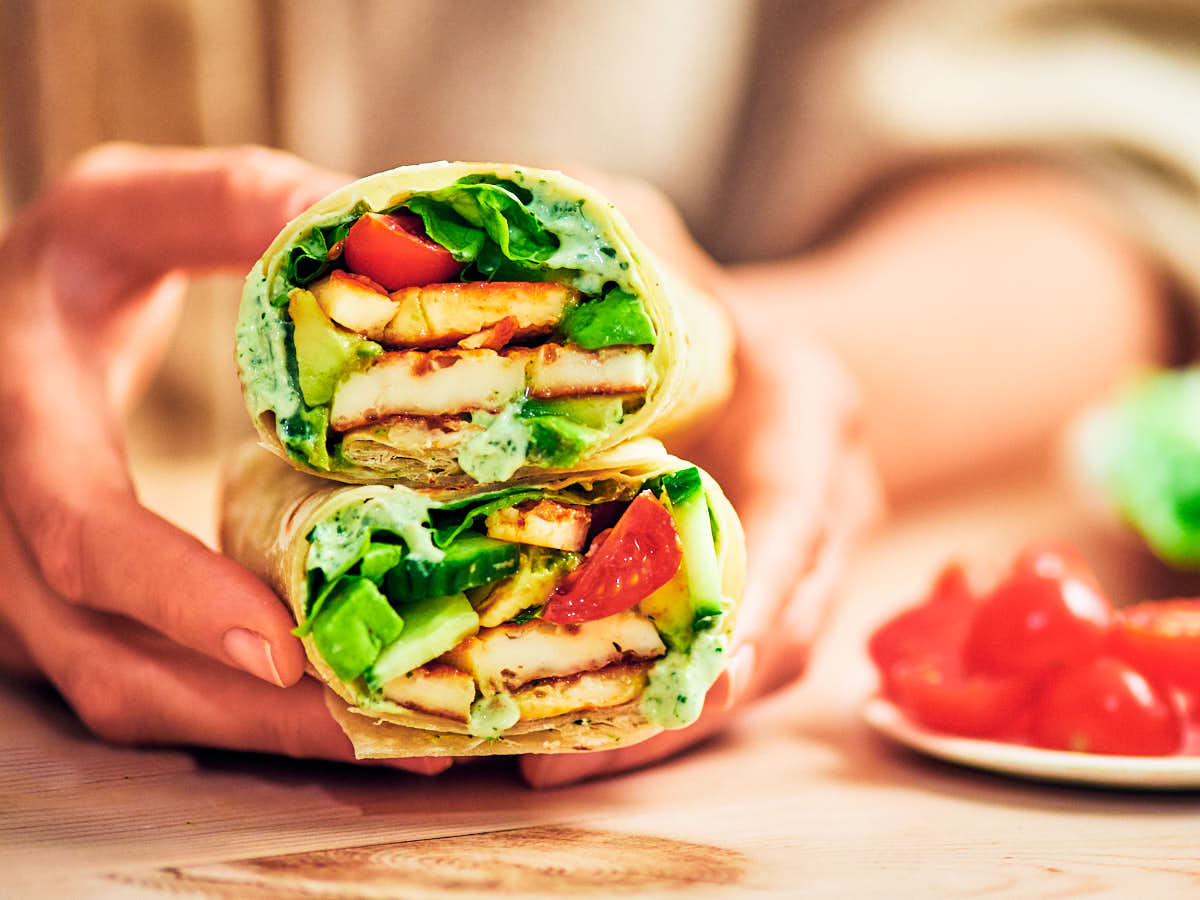 A woman's hands holding Halloumi wraps with hot honey over a table.