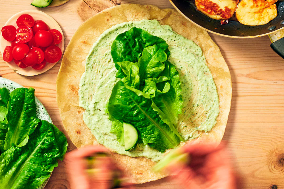 Assembling wraps with sauce and fresh veggies on a wooden table.