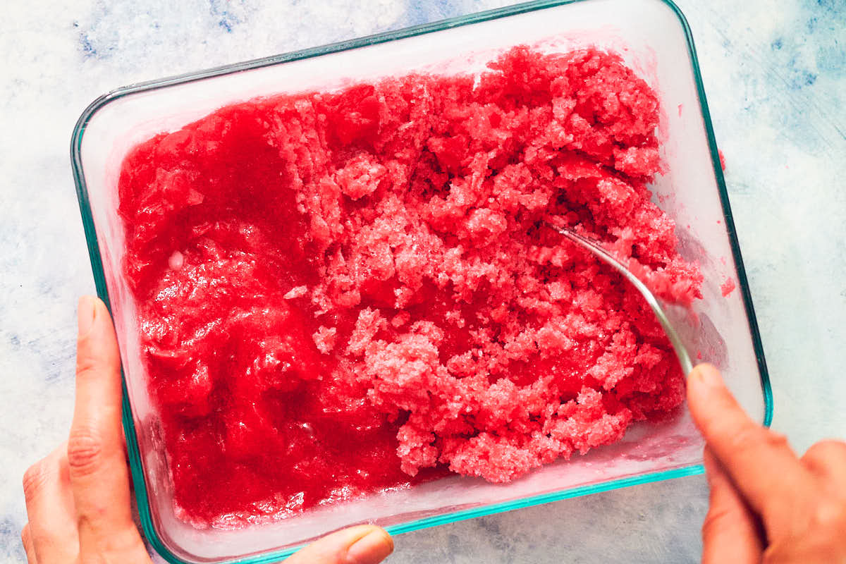 A fork scraping frozen strawberry rhubarb granita before serving.