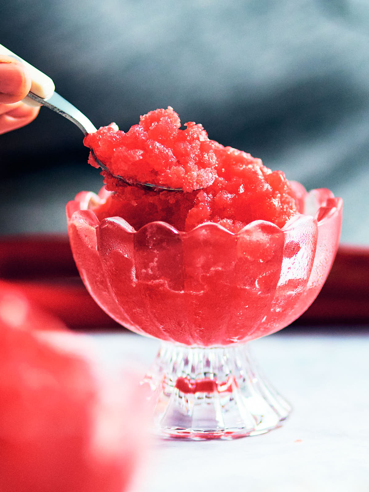 A spoon scooping Strawberry Rhubarb Granita from a glass bowl.