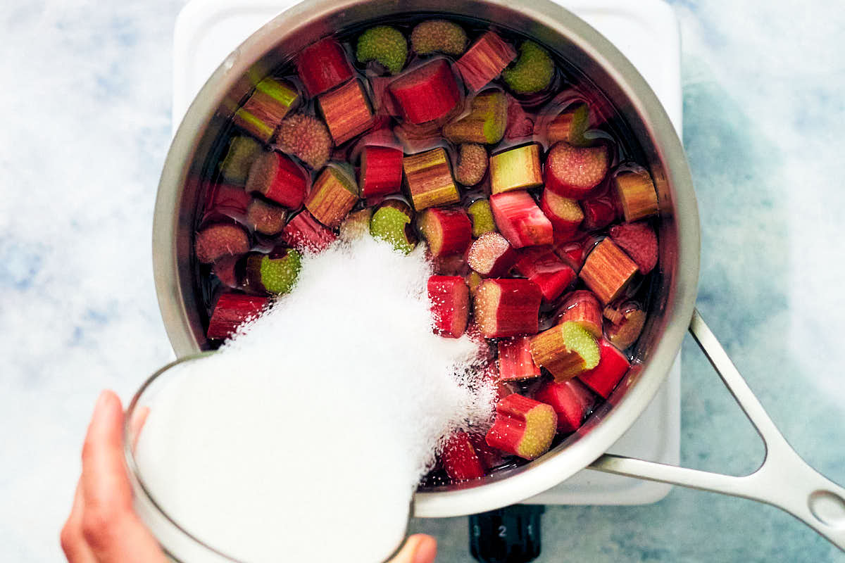 Sugar being poured over chopped rhubarb in a sauce pan.