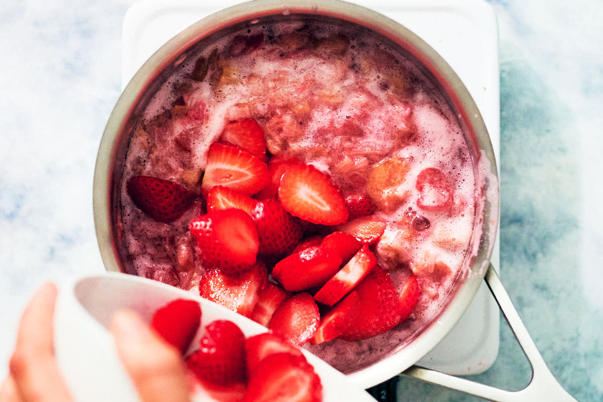 Sliced strawberries being added to a pot of simmering rhubarb compote.