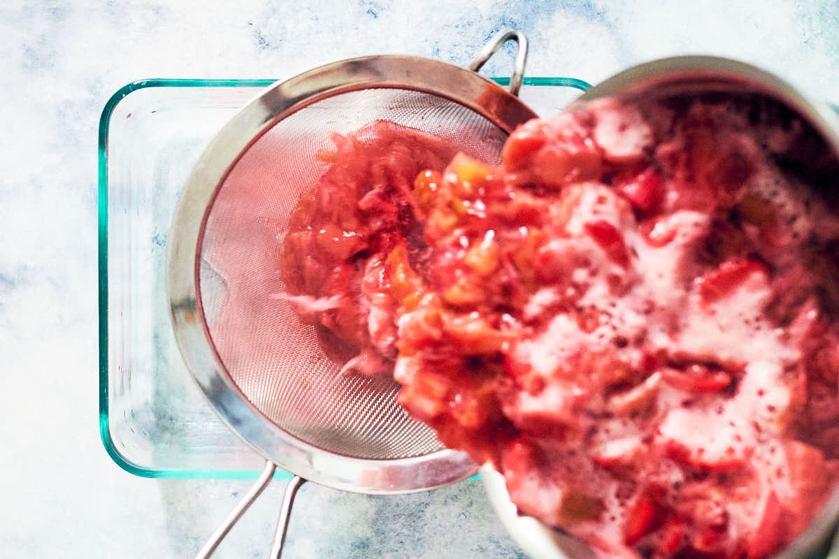 Pouring strawberry rhubarb mixture into a fine mesh sieve to strain.