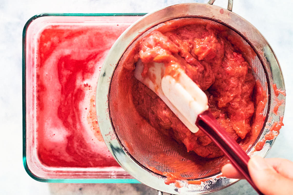 Stewed strawberries and rhubarb being pressed through a fine mesh sieve to extract juice. 