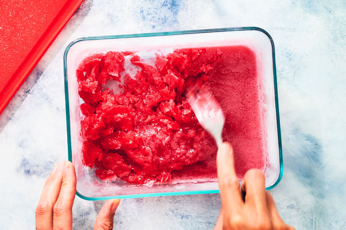 A fork scraping partially frozen strawberry rhubarb granita,