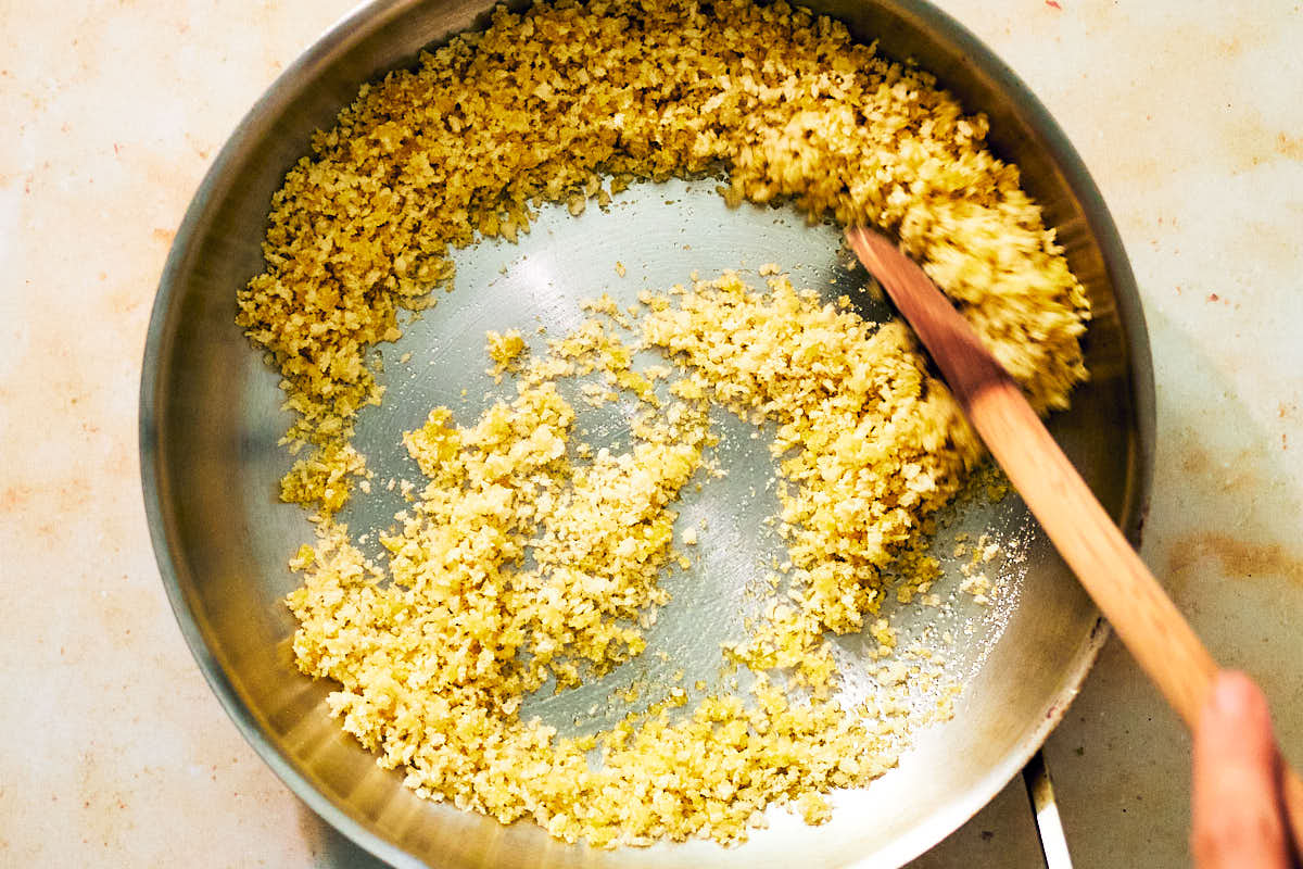 Panko breadcrumbs being stirred with a wooden spoon in a skillet.