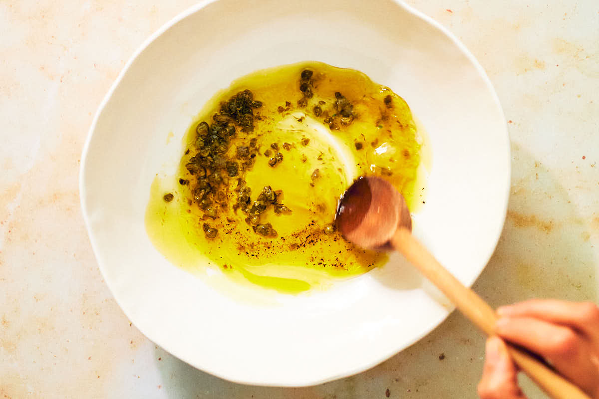 Mixing olive oil, capers, and lemon juice in a bowl for salad dressing.