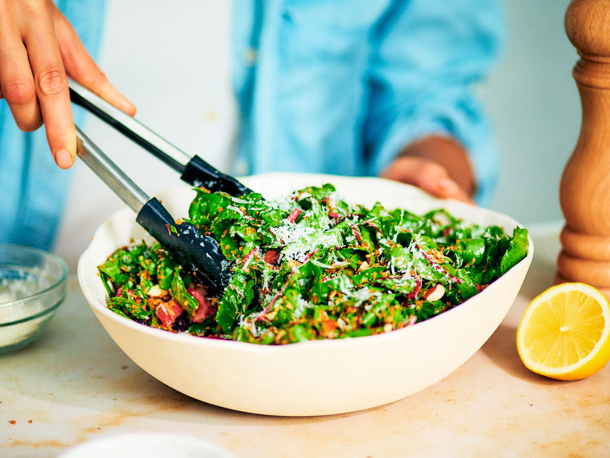 A woman serving swiss chard salad out of a bowl.