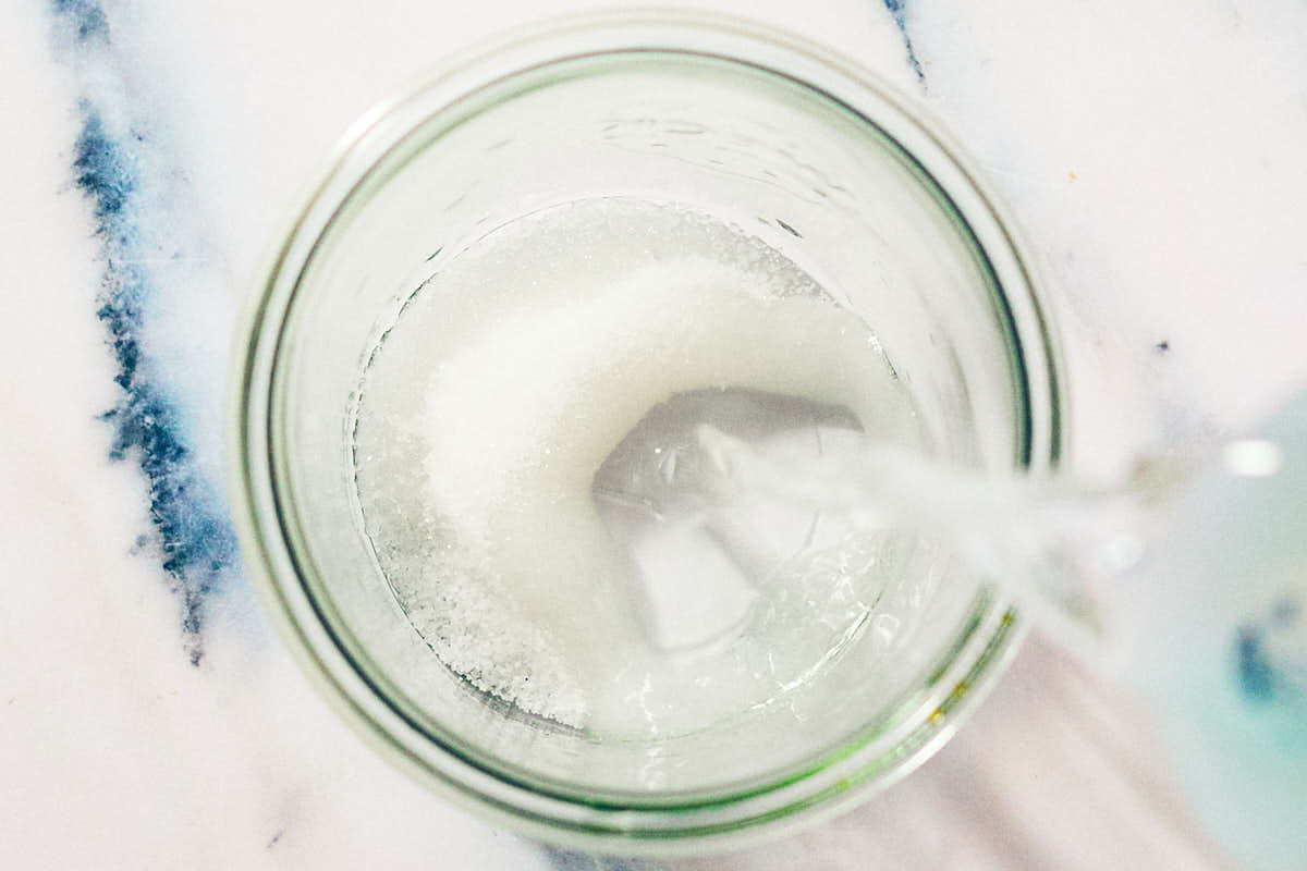 Hot water being poured into a glass jar with sugar and salt for pickling brine.