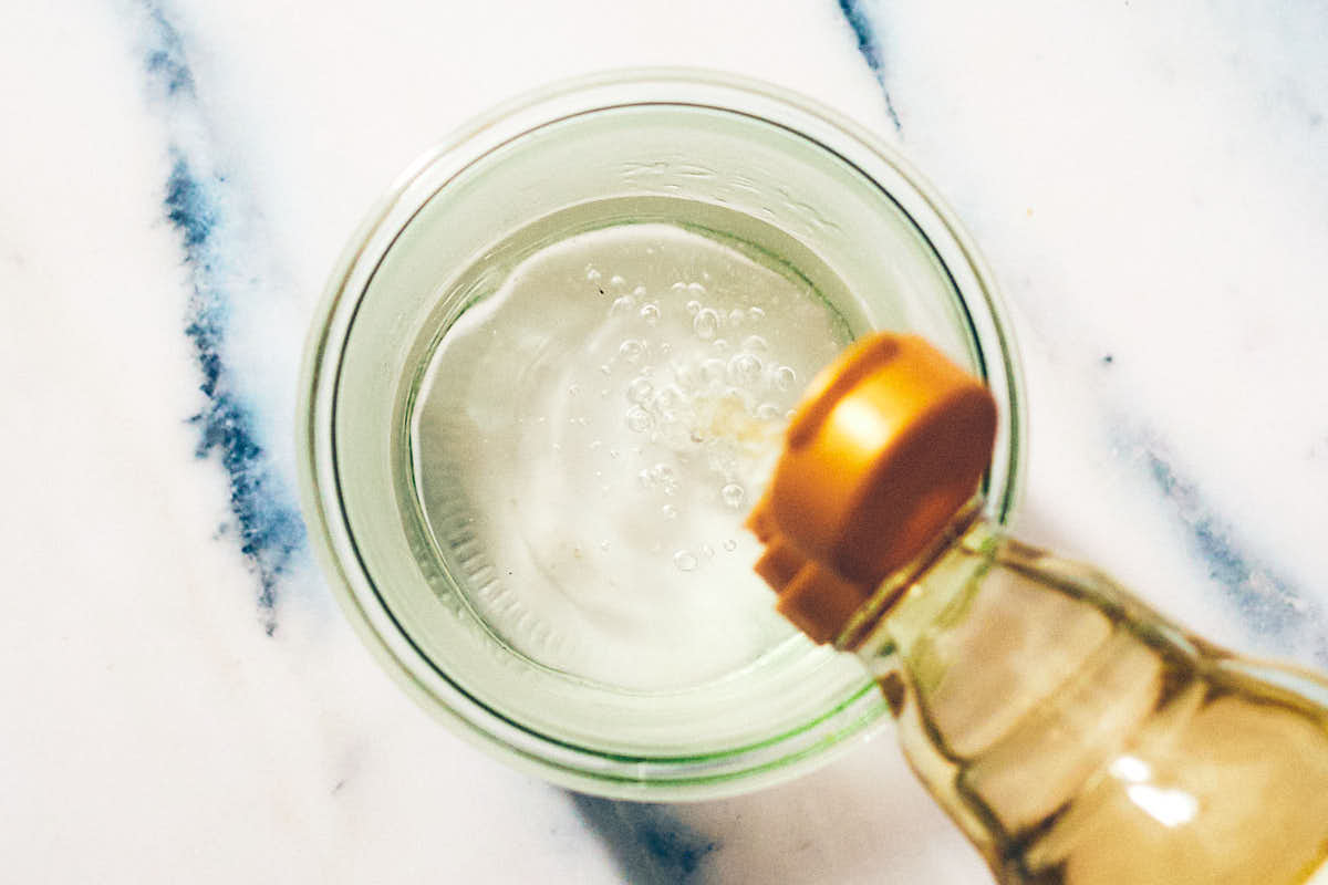 Rice vinegar being poured into a glass jar to make pickling brine.