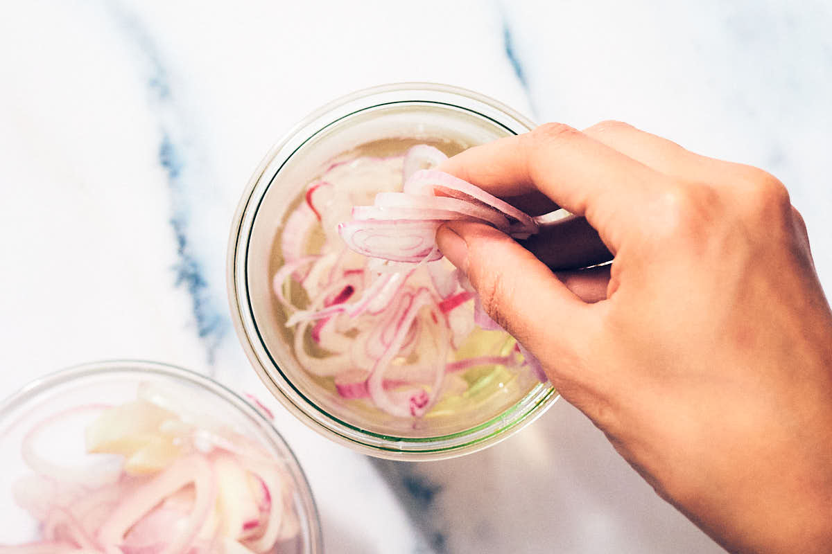 Thinly sliced shallots being added to vinegar brine to quick pickle.