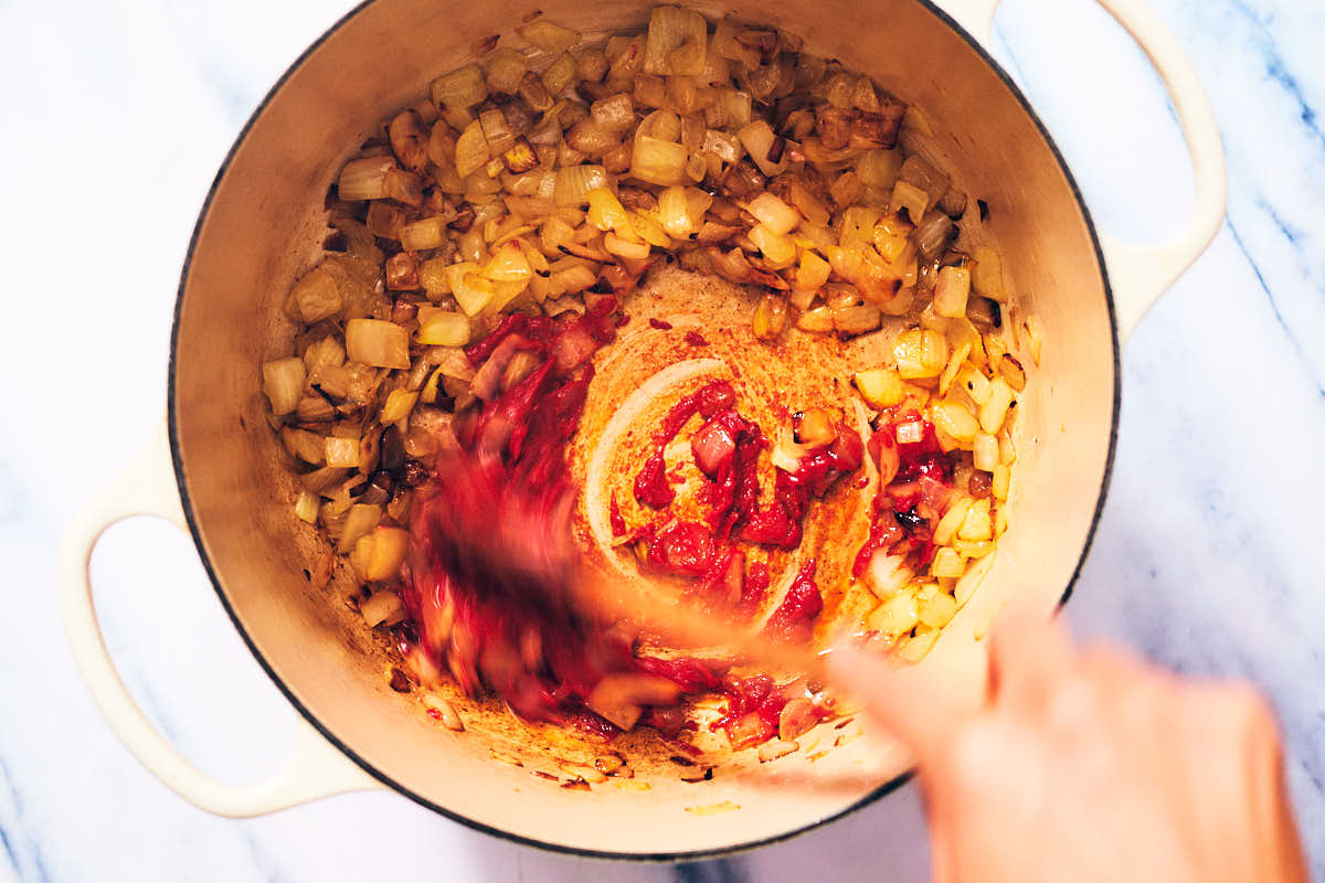 Onions and tomato paste being stirred in a pot for ratatouille pasta.