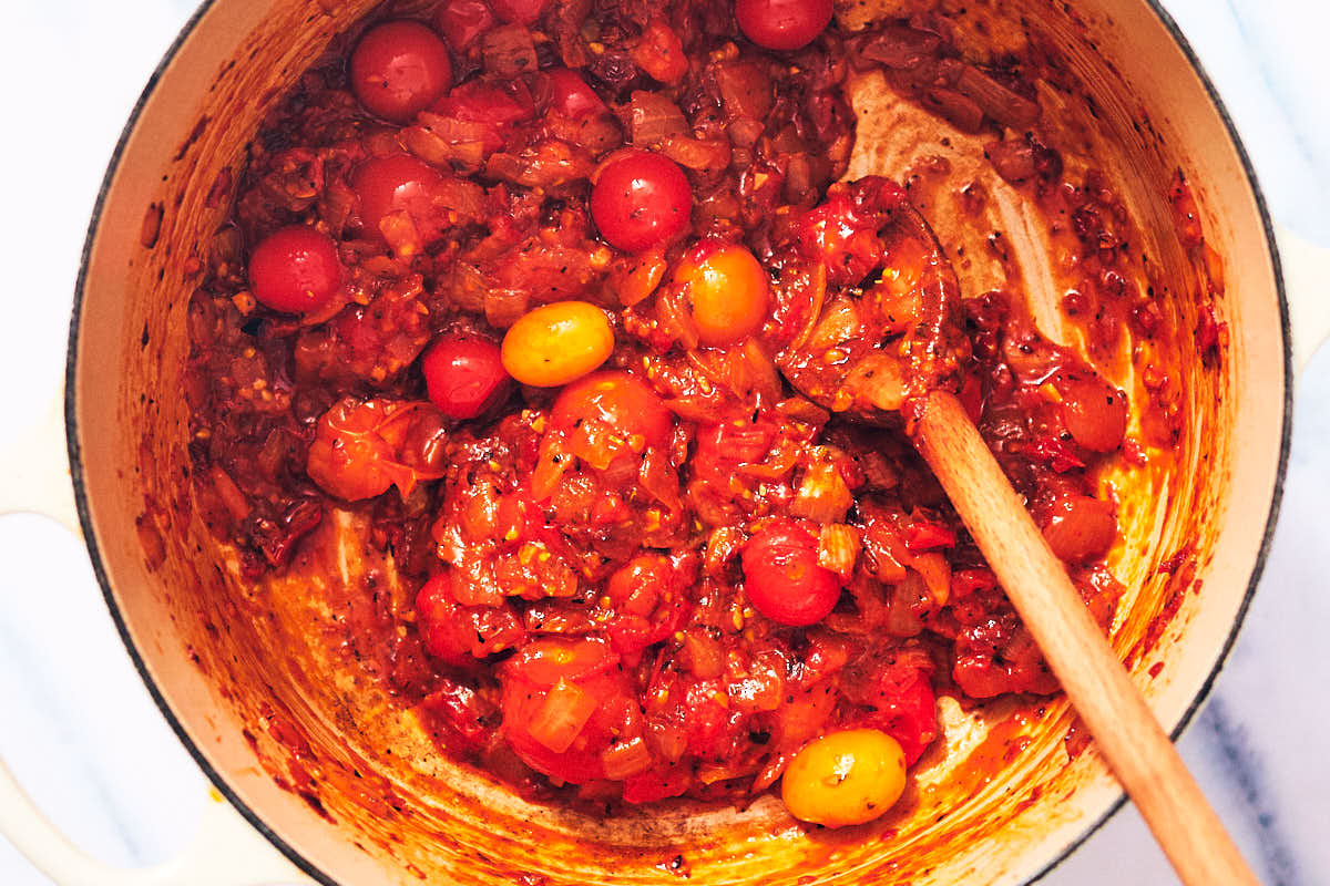 Jammy tomatoes and onion in a pot with a wooden stirring spoon.