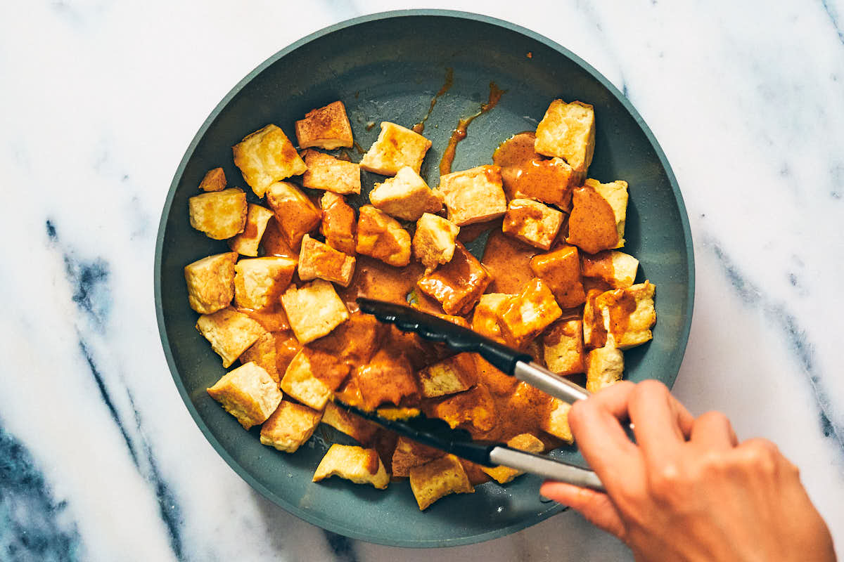 Cubed tofu being tossed with tofu seasoning for vegan satay recipe.