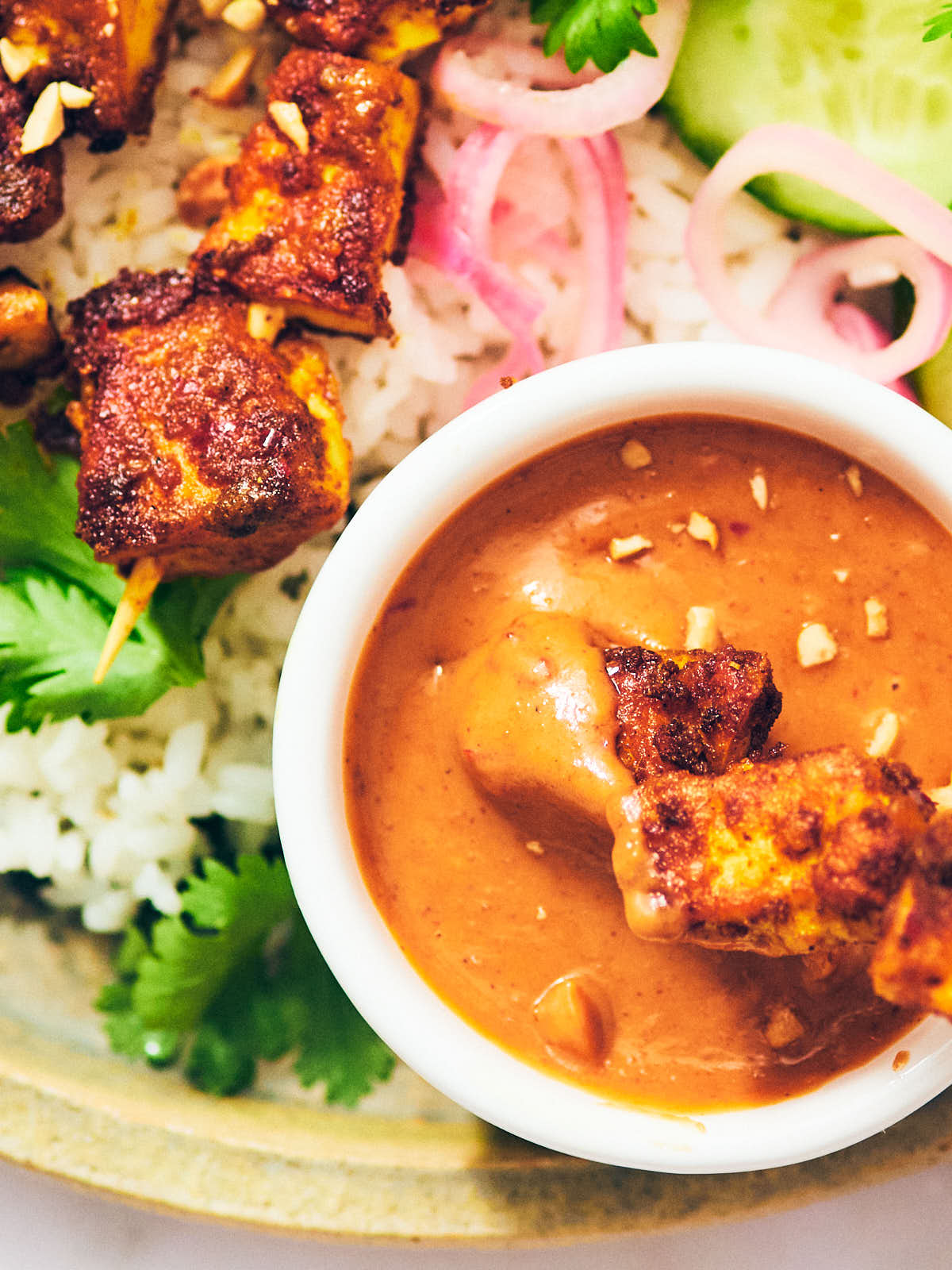 Dipping tofu satay skewers into peanut sauce.