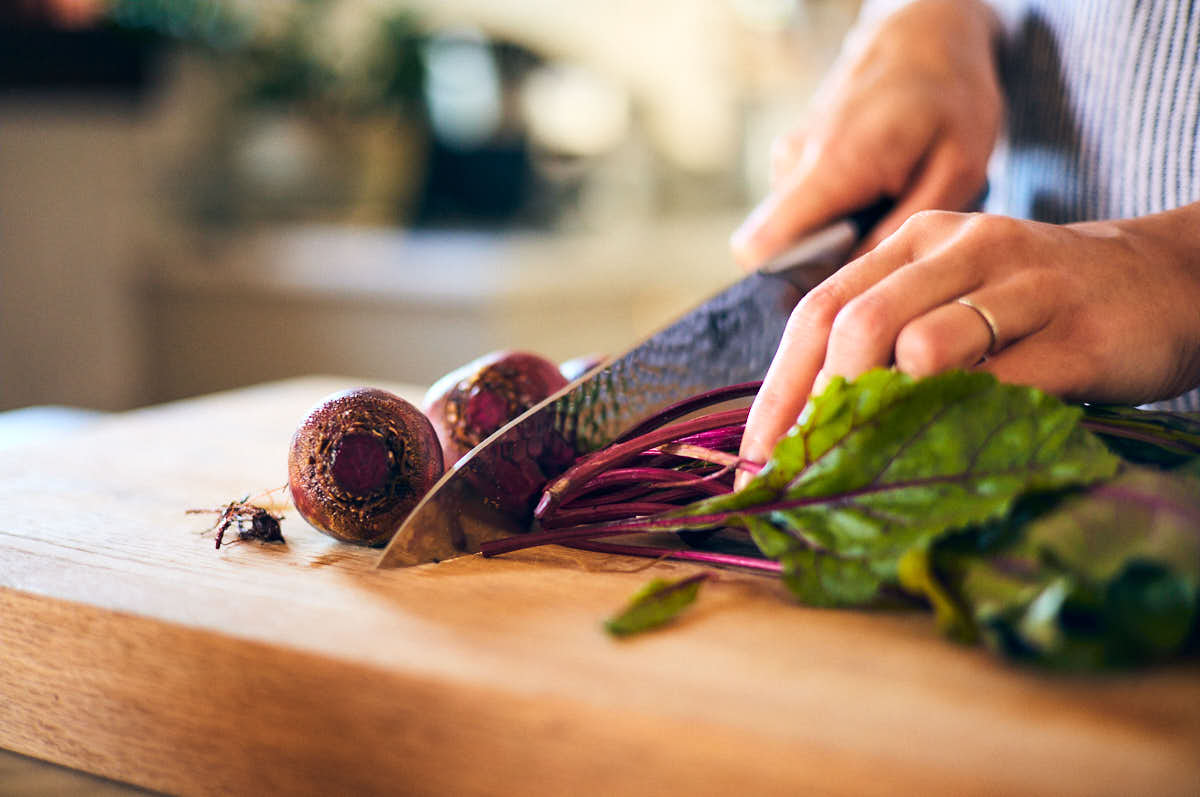 A knife trimming off the ends of raw beets on a cutting board.