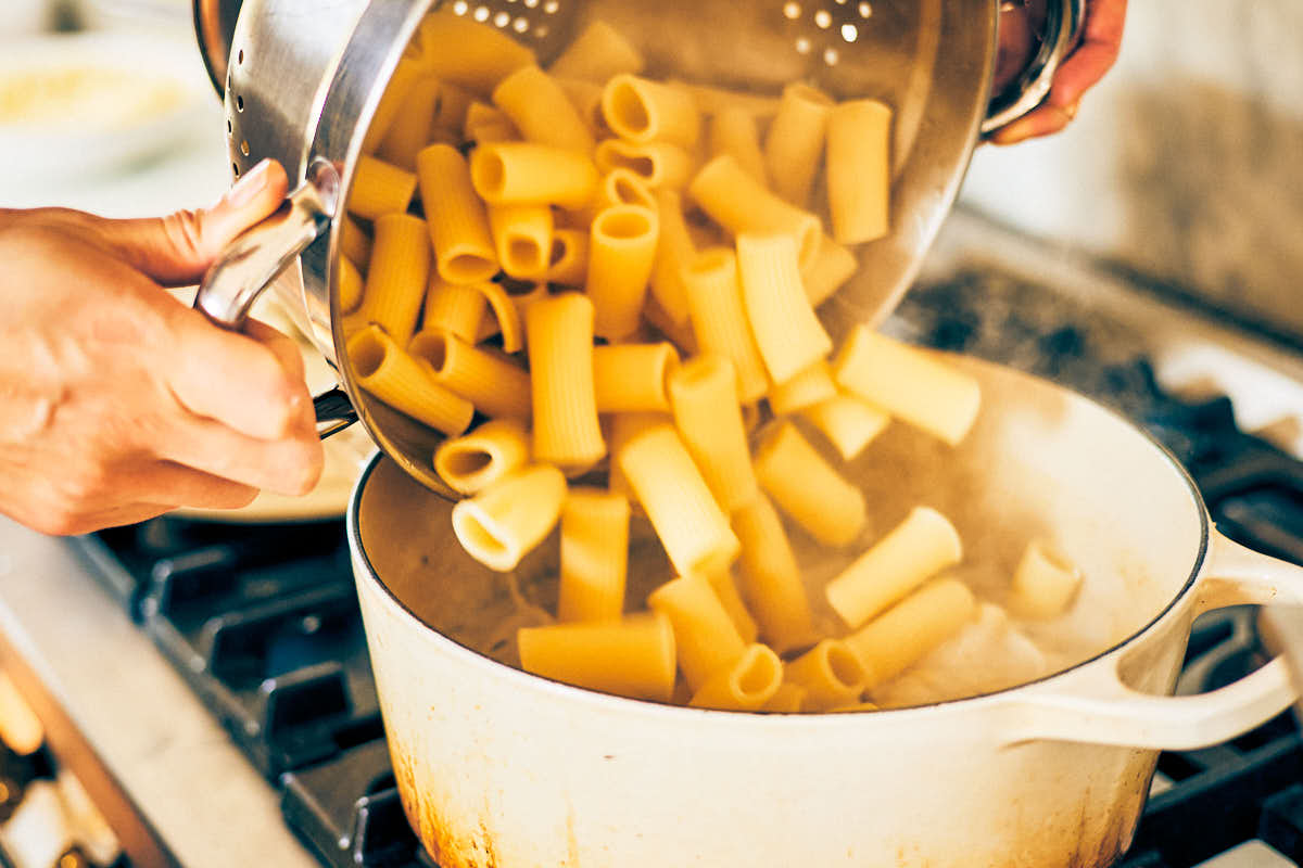 Cooked pasta being added to a pot of garlic herb sauce.