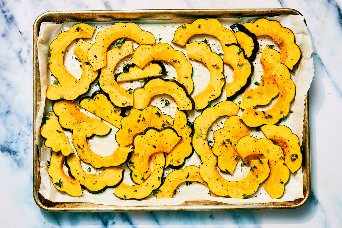 Sliced acorn squash on a baking sheet before roasting.