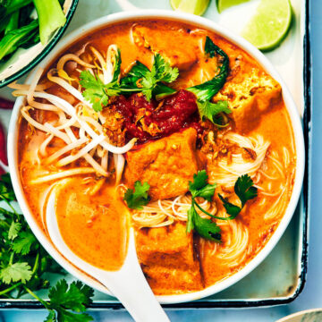 Vegan Laksa Soup with noodles and tofu in a bowl with a spoon.