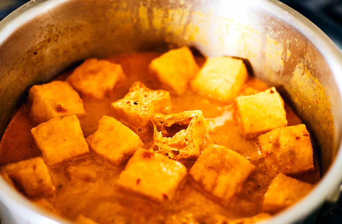 Fried tofu puffs simmering in a pot of laksa soup.