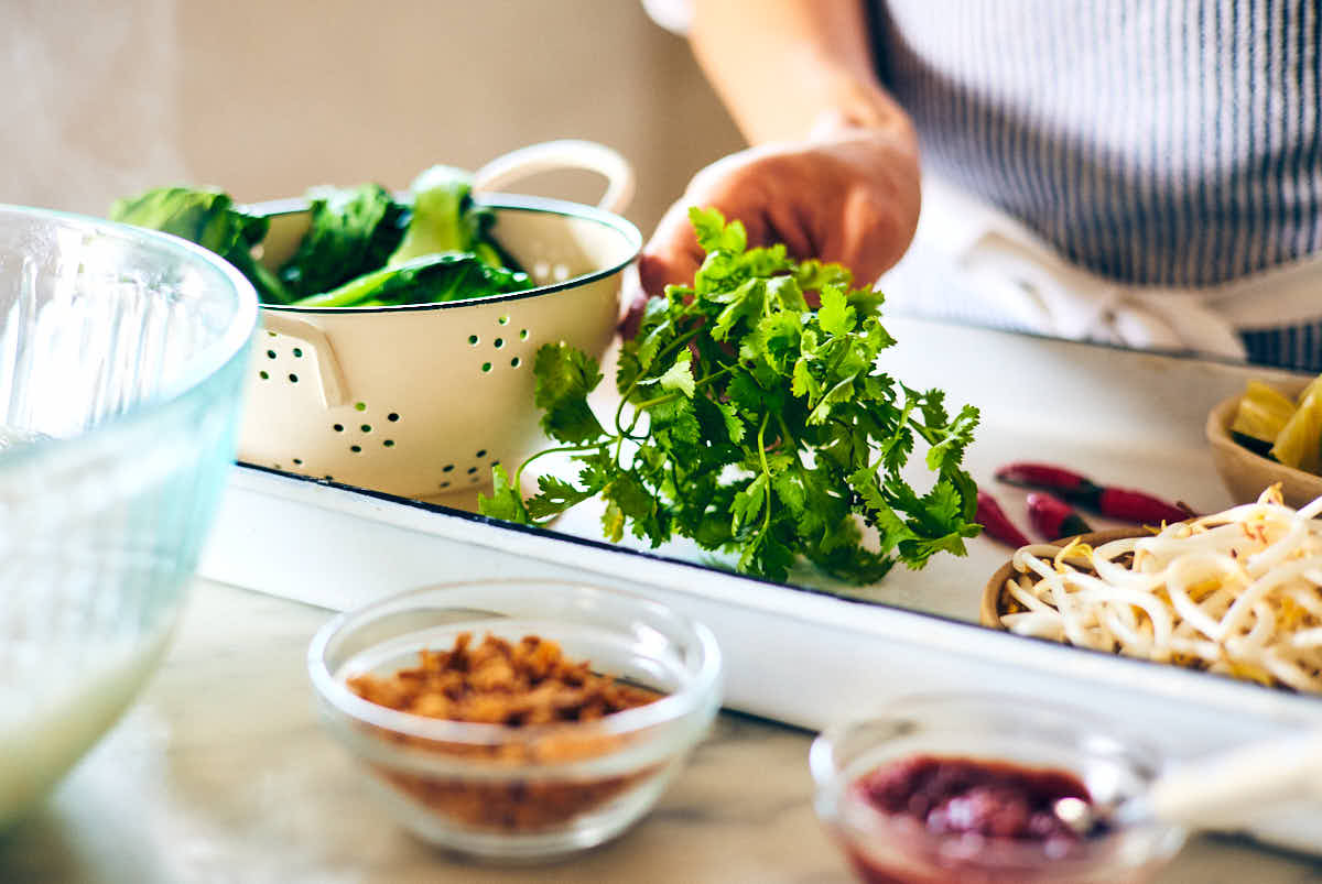 A woman preparing toppings to serve with vegan laksa.