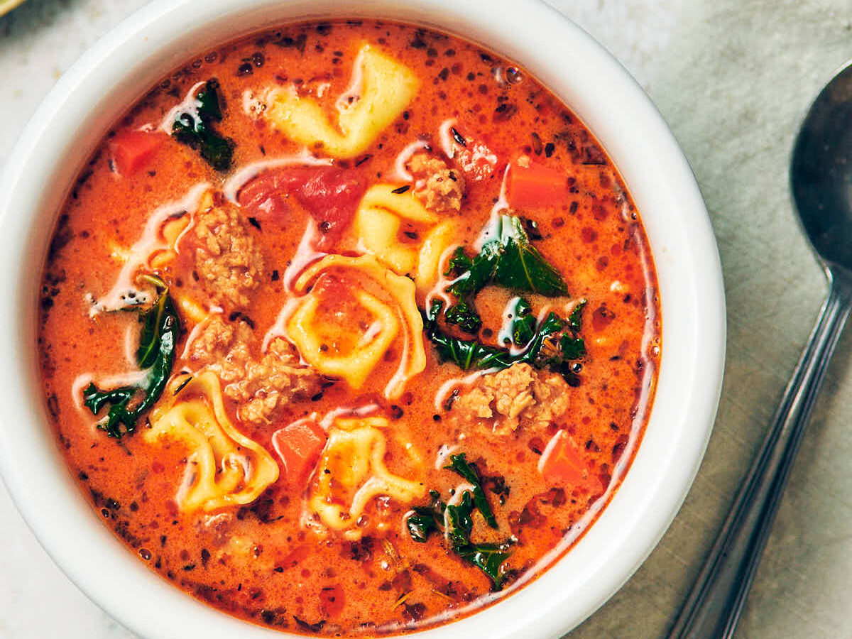 A bowl of creamy vegetarian tortellini soup with kale and plant based sausage.