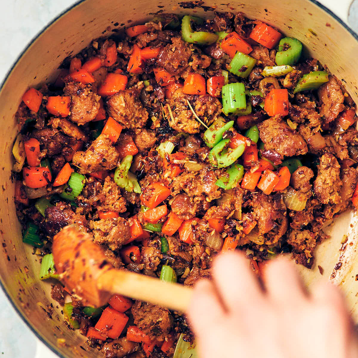 Carrots, celery, garlic, and spices being stirred into a pot of crumbled sausage for Tortellini Soup.