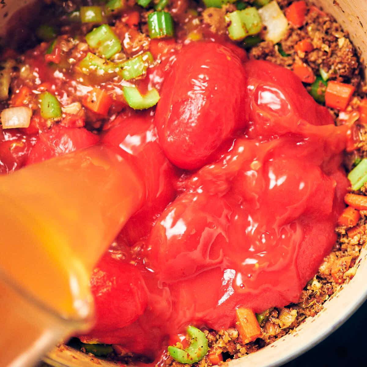 A pot with sauteed veggies, plant based sausage, canned whole tomatoes, and vegetable broth.