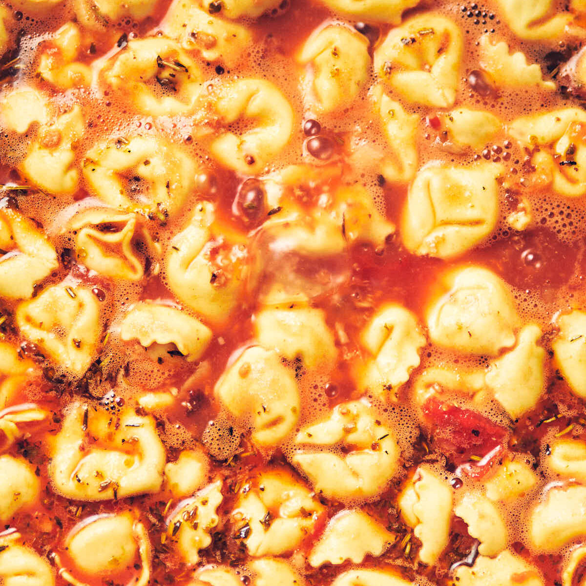 Tortellini being cooked in a pot of tomato veggie soup.