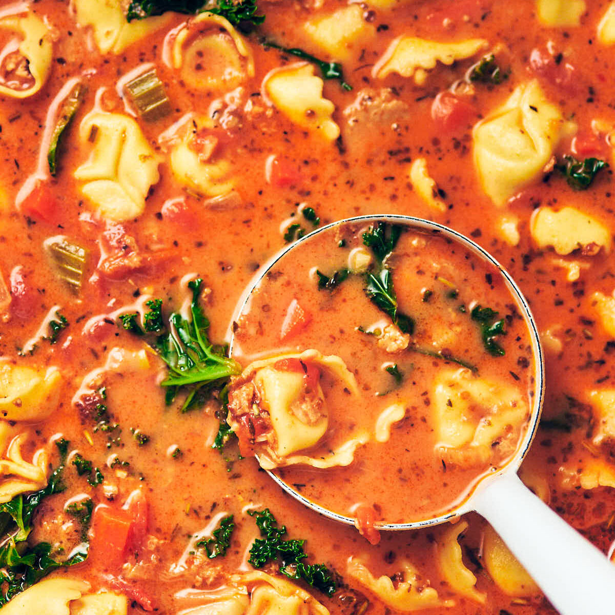 A ladle scooping Creamy Vegetarian Tortellini Soup with Kale out of the pot to serve for dinner.