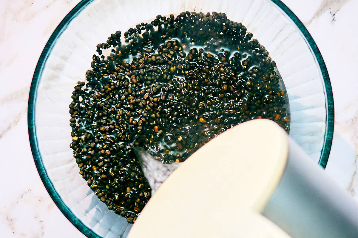 Boiling water being poured over a bowl of black gram (whole urad dal).