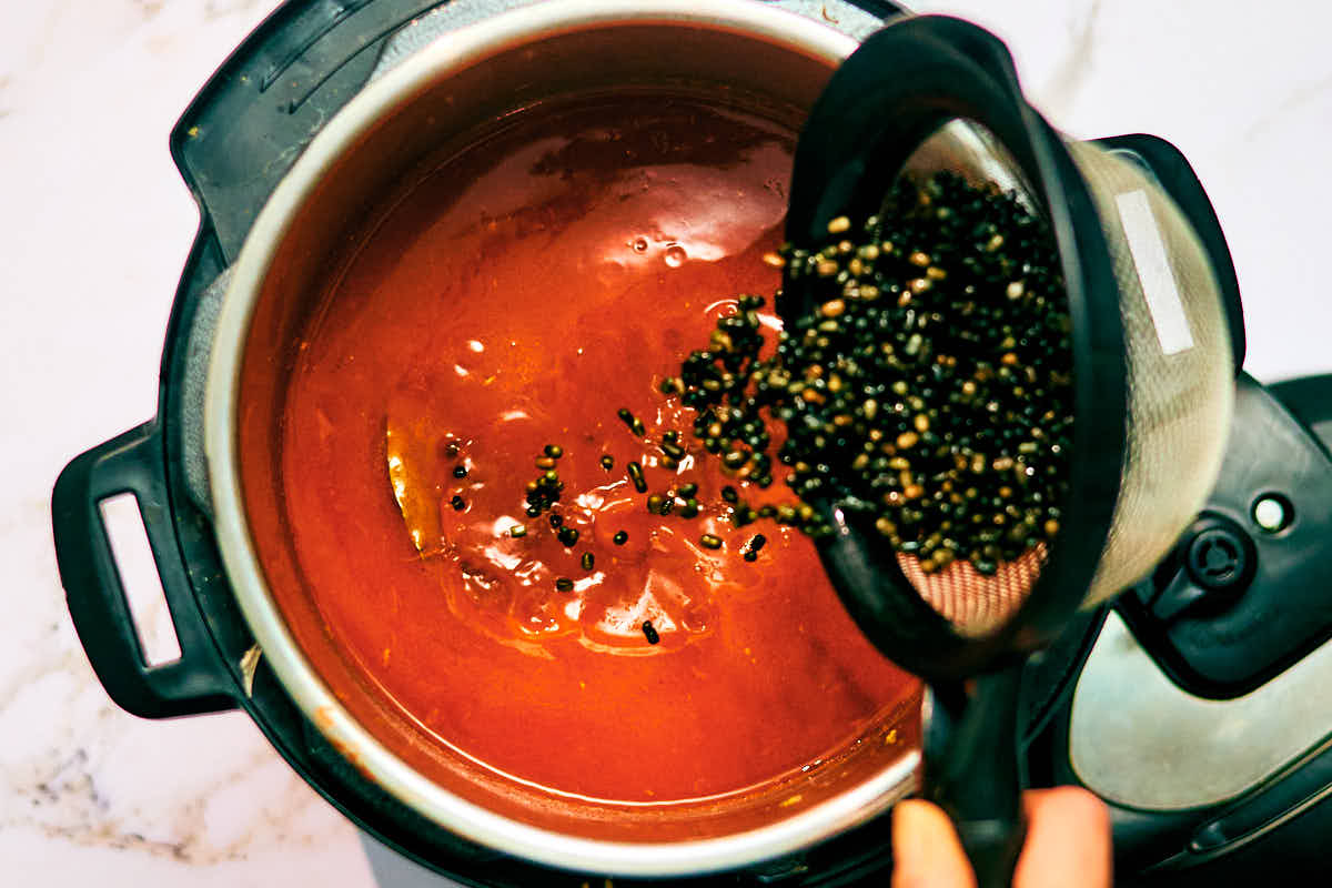 Whole black dal (Urad dal) being added to an Instant Pot with ingredients for Dal Makhani.